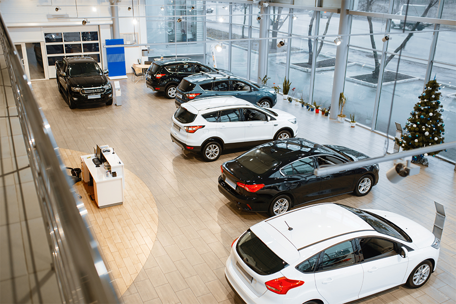 In einem modernen Autohaus werden mehrere neue Autos, sowohl in Schwarz als auch in Weiß, in Reihen auf einem gefliesten Boden in der Nähe großer Fenster aufgestellt. In der Ecke steht ein geschmückter Weihnachtsbaum.