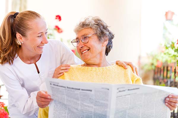 Frau liest Zeitung und lächelt andere Frau an, Beleuchtung Krankenhaus