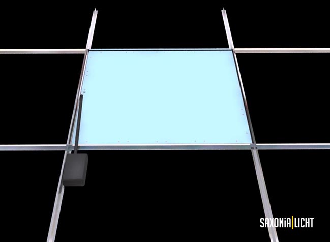 Eine quadratische blaue LED-Panelleuchte ist in einer Metallrahmenstruktur vor schwarzem Hintergrund montiert. Das Panel, das moderne LED-Technik verwendet, ist an seiner linken Seite mit einem kleinen rechteckigen schwarzen Bauteil verbunden. In der unteren rechten Ecke ist der Text „Saxonia Licht“ des renommierten Leuchtenherstellers zu sehen.