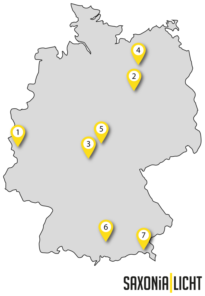 Eine Deutschlandkarte mit sieben gelben Standortnadeln, die jeweils von 1 bis 7 nummeriert sind. Der Hintergrund ist schwarz und die durch die Nadeln dargestellten Regionen oder Städte sind nicht beschriftet. In der unteren rechten Ecke befindet sich ein Logo von „SAXONIA LICHT“, bekannt für seine LED-Beleuchtungssysteme.